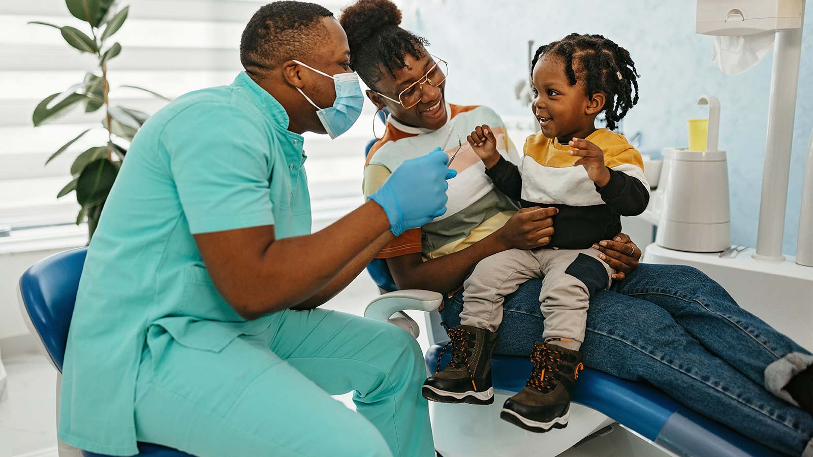 Dentist giving child dental exam while he sits on his mother's lap.