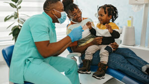 Dentist giving child dental exam while he sits on his mother's lap.