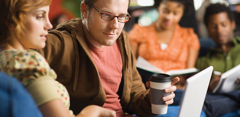 Man and woman sit together looking at their laptop in a public space.