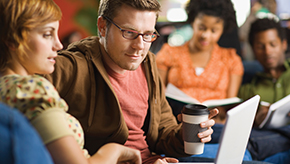 Man and woman sit together looking at their laptop in a public space.