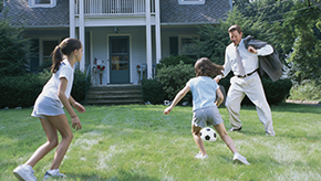 A dad plays soccer with his two daughters in the front yard of their house after he gets home from work.