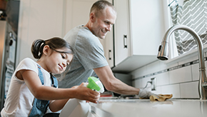 A dad and daughter clean dishes together at the kitchen sink