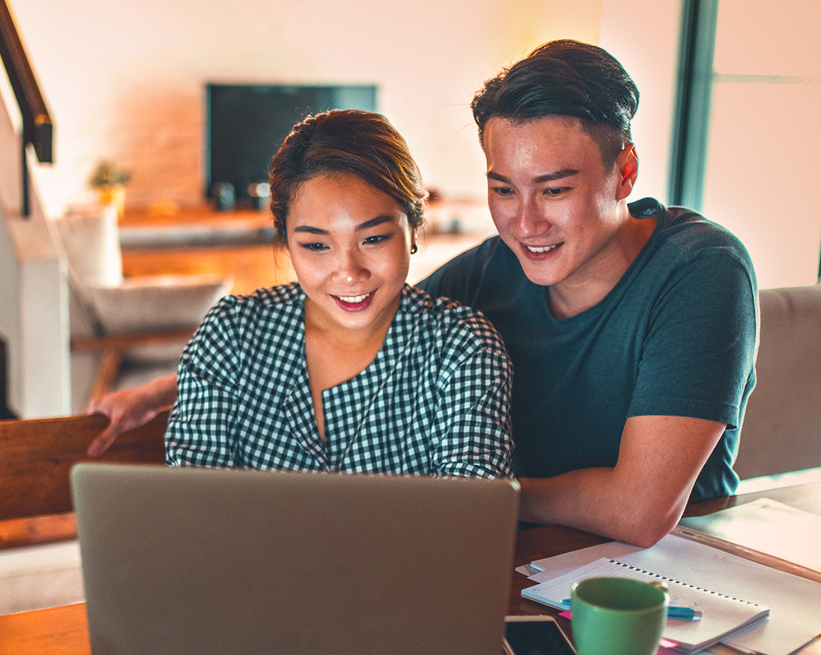 Smiling man and woman sitting at table looking at a laptop.