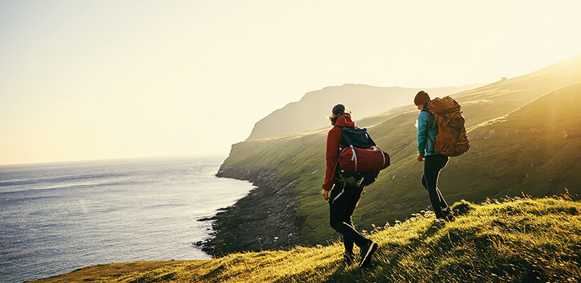 Two friends hiking along a peaceful seaside cliff as the sun rises behind them.