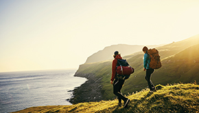 Two friends hiking along a peaceful seaside cliff as the sun rises behind them.