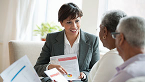 A financial professional is holding a document and happily explaining to two of her retired clients how to reach their goals of financial stability.