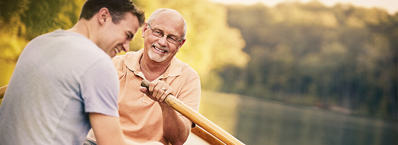 A grandfather shares a laugh with his teenage grandson while rowing a small boat on a lake on a sunny, spring day.