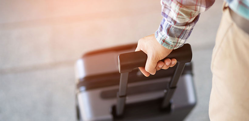 A hand pulling a carry-on piece of luggage.