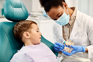African American dentist teaching small boy how to brush teeth properly during dental appointment.