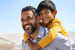 Happy smiling indian father giving son ride on back
