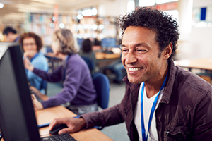 Group Of Mature Adult Students In Class Working At Computers In College Library