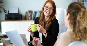 Female laughing and having a cup of coffee with another female.