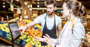 Employee helping female weigh produce on a scale at a super market.