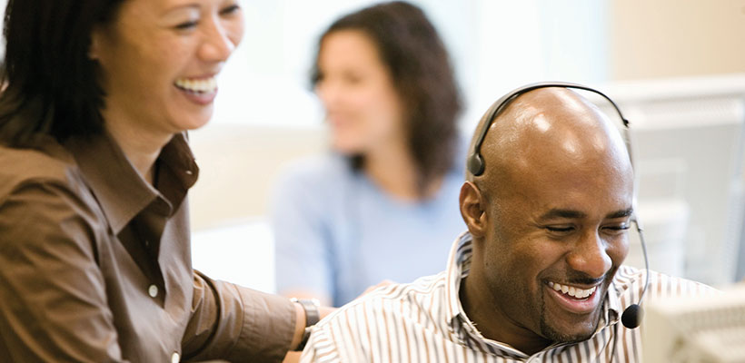 Female and male laughing while at work and looking at a computer screen.