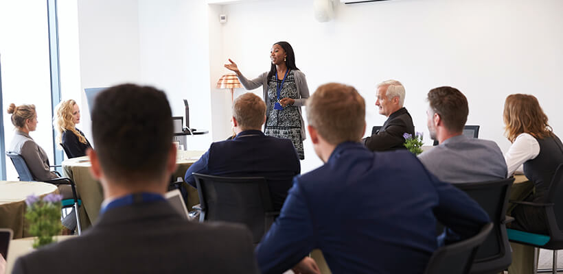 A female leading a classroom of business colleagues.