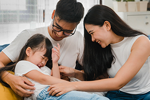 Happy Asian couple playing with their daughter on sofa.