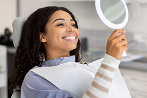 Happy female patient looking at a mirror in dental chair.