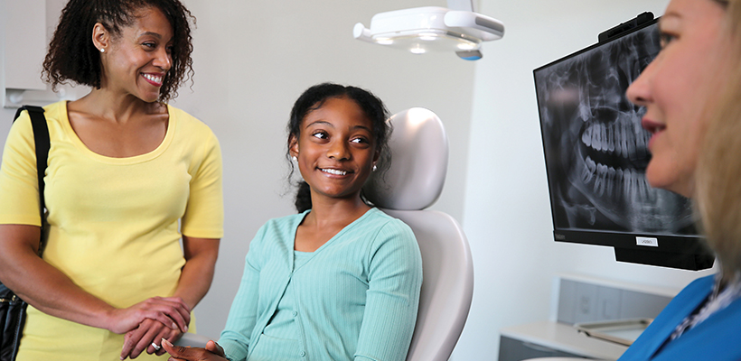 Young girl sitting in dental chair with her mother by her side, ready to talk with the dentist.