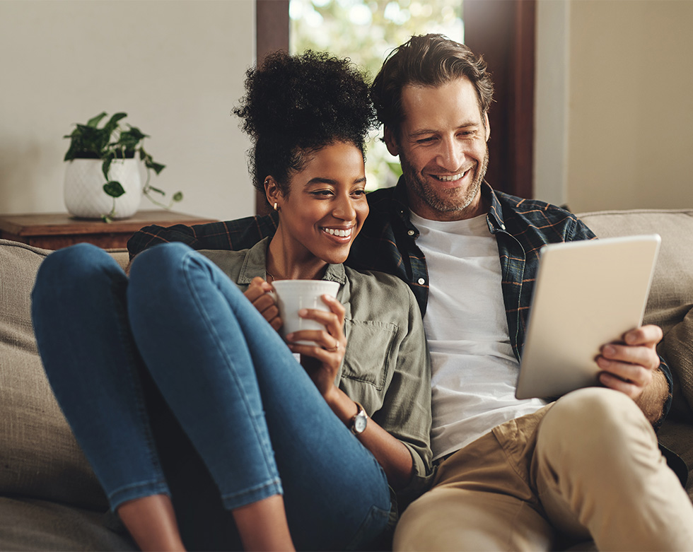 Happy young couple using digital tablet together on couch