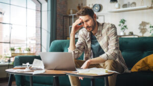 Stressful Accounting at Home: Man Using Laptop, Filling Tax Forms. Worried Male Has Paperwork Problems with Bills and Invoices. Budget Deficit, High Inflation, Financial Difficulty, Debt, Bankruptcy