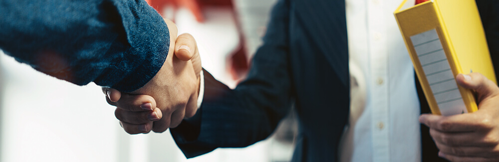 B_140_2018_1000x325 Two business associates shaking hands.
