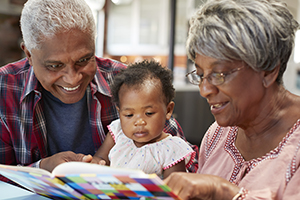 Grandparents Reading Book With Baby Granddaughter At Home