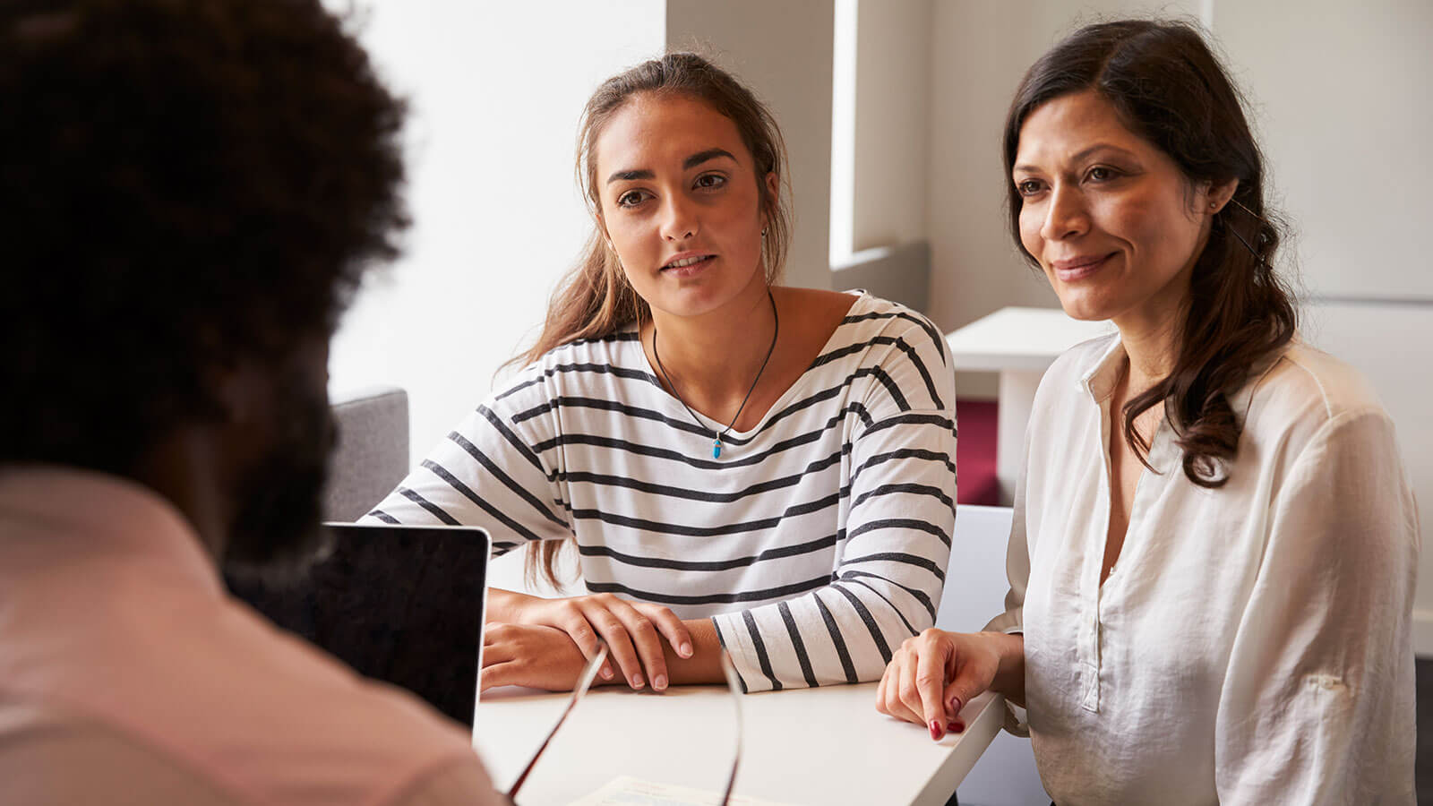 A young woman and her mother meeting with a college admissions counselor.