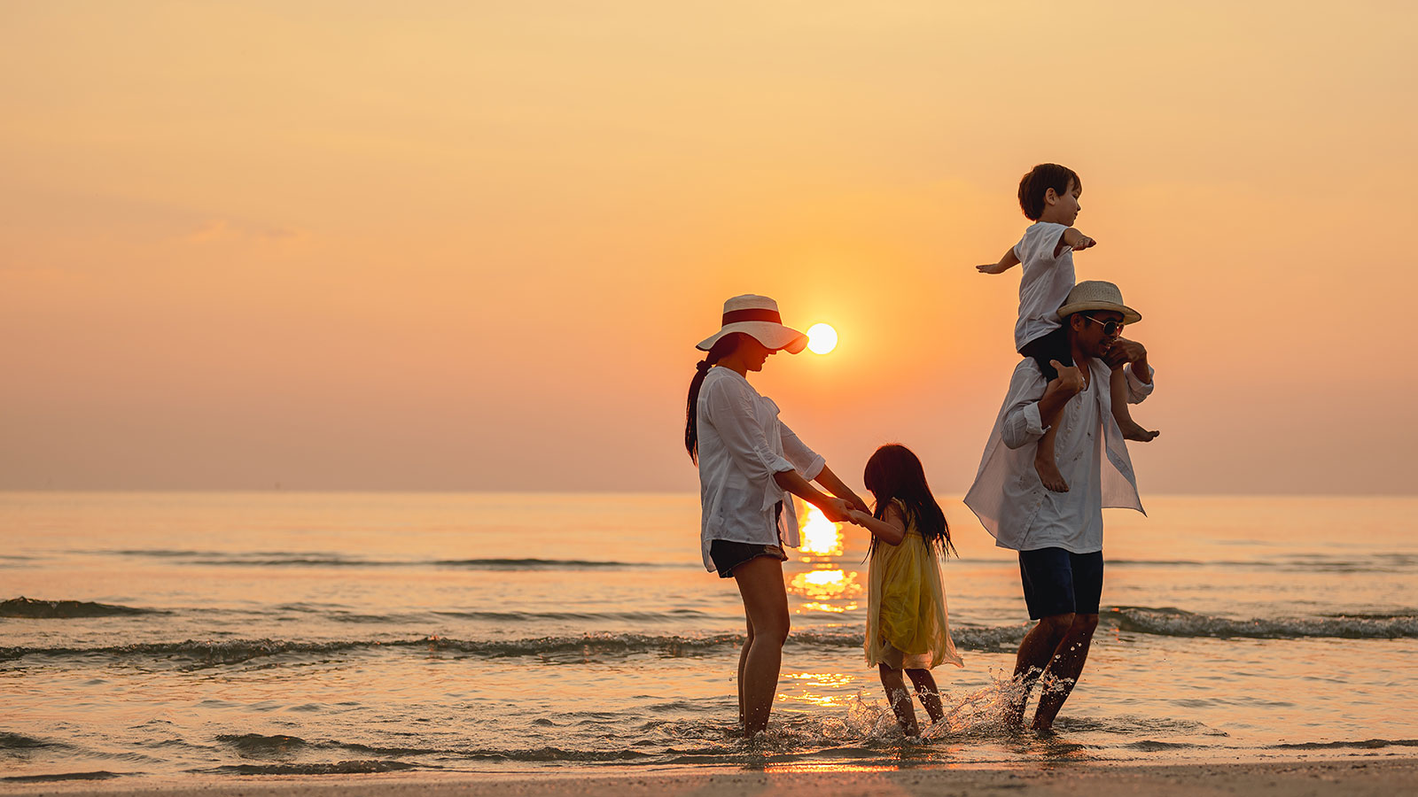 A mom and dad play with their young son and daughter on the beach at sunset. They’re relaxed knowing they’re using life insurance in their financial strategy.
