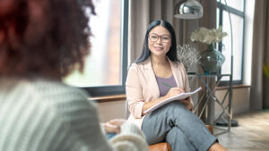 Two females sitting in chairs discussing why employee mental health benefits are essential.