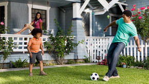 Two brothers kicking a soccer ball on the front lawn of their home.