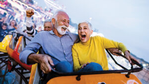 A husband and wife excitedly laugh while on a rollercoaster enjoying their retirement adventures.