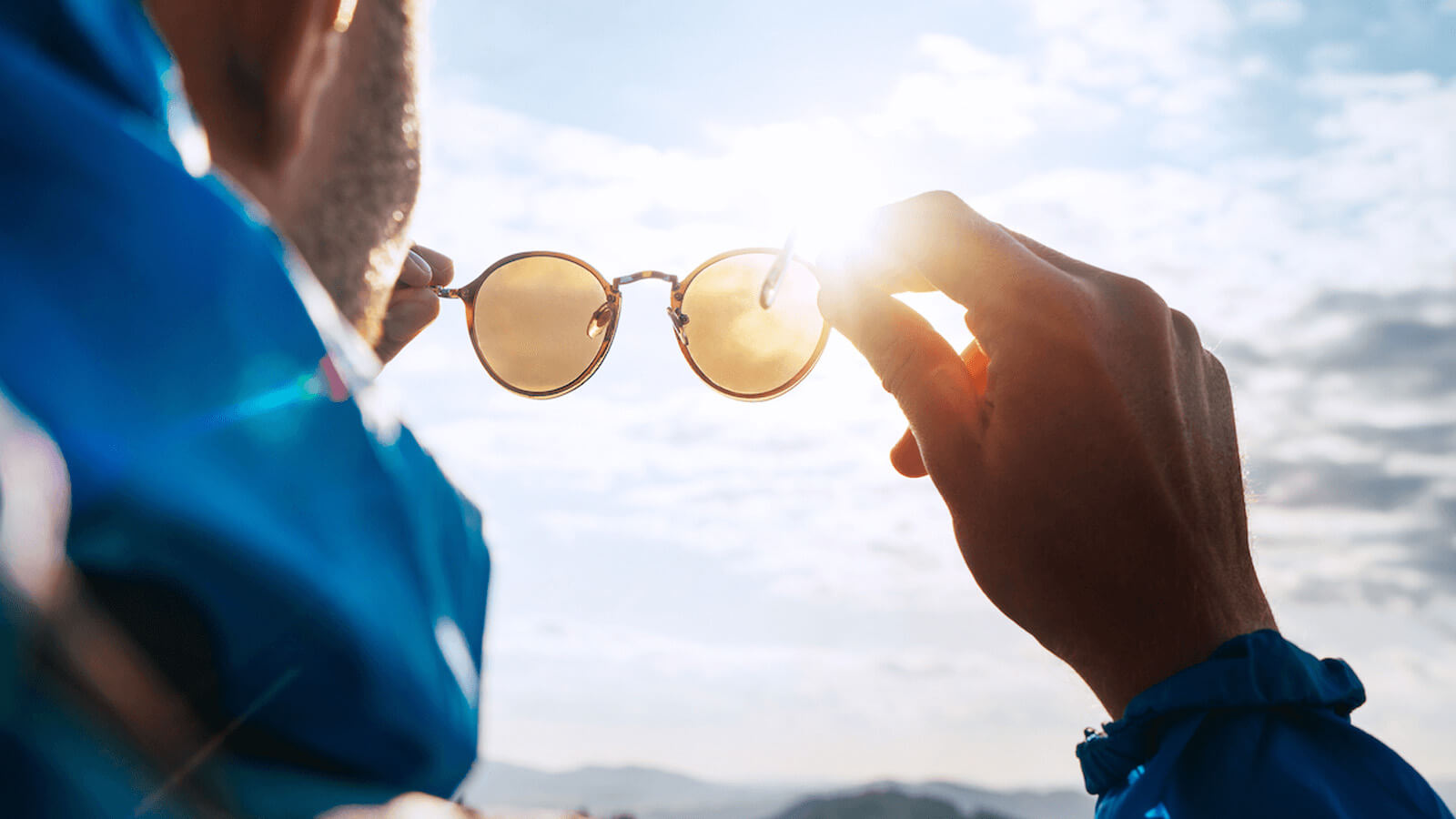 Male holding a pair of sunglasses and looking up at the sky.