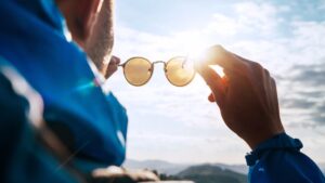 Male holding a pair of sunglasses and looking up at the sky.