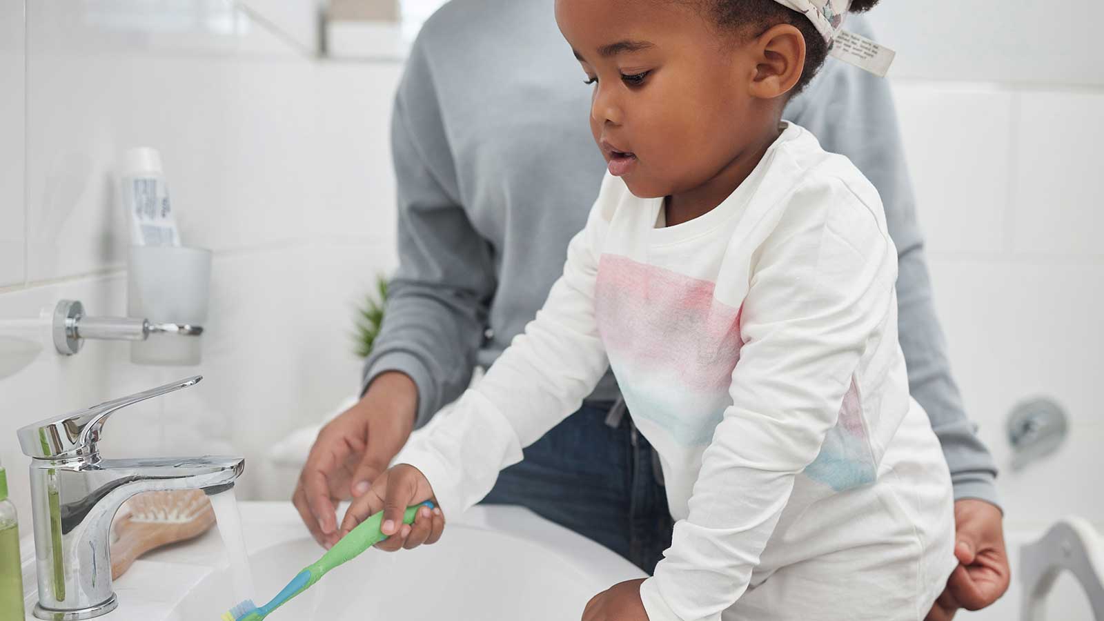 Young girl rinsing toothbrush under water at the sink.