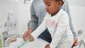 Young girl rinsing toothbrush under water at the sink.