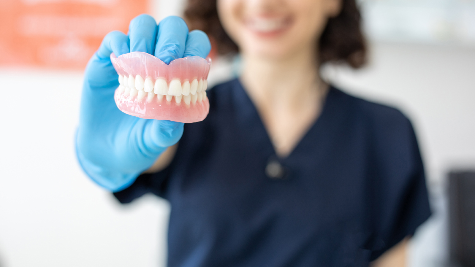 Dental hygienist smiling while holding and up close shot of dentures.