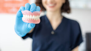 Dental hygienist smiling while holding and up close shot of dentures.