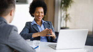 A young professional woman looks at her laptop screen while meeting with a financial professional to learn how to start investing.