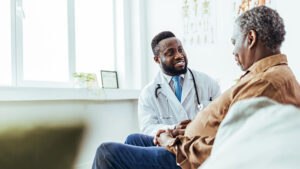 A man in his 70s meets with his doctor to discuss his ongoing treatment and thinks about how he’s going to pay for a serious illness in his retirement years.