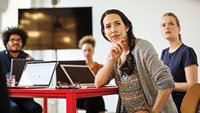 Female standing at desk with laptop looking away.