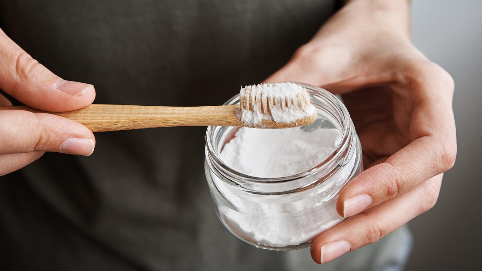 Individual holding a jar of baking soda and a toothbrush. Individual holding a jar of baking soda and a toothbrush.
