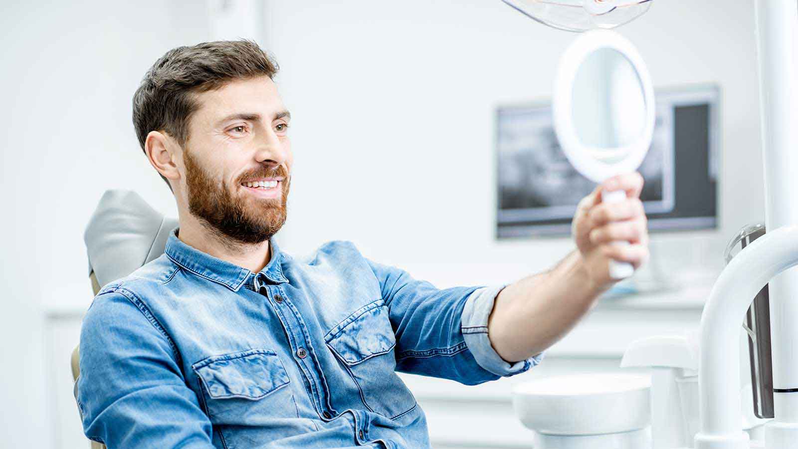 Man with beard smiling looking in mirror while sitting in dental chair. Man with beard smiling looking in mirror while sitting in dental chair.