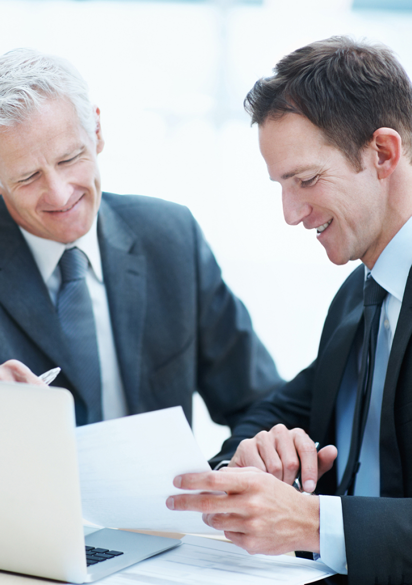 Two male colleagues sitting at a table with a laptop discussing business. Two male colleagues sitting at a table with a laptop discussing business.