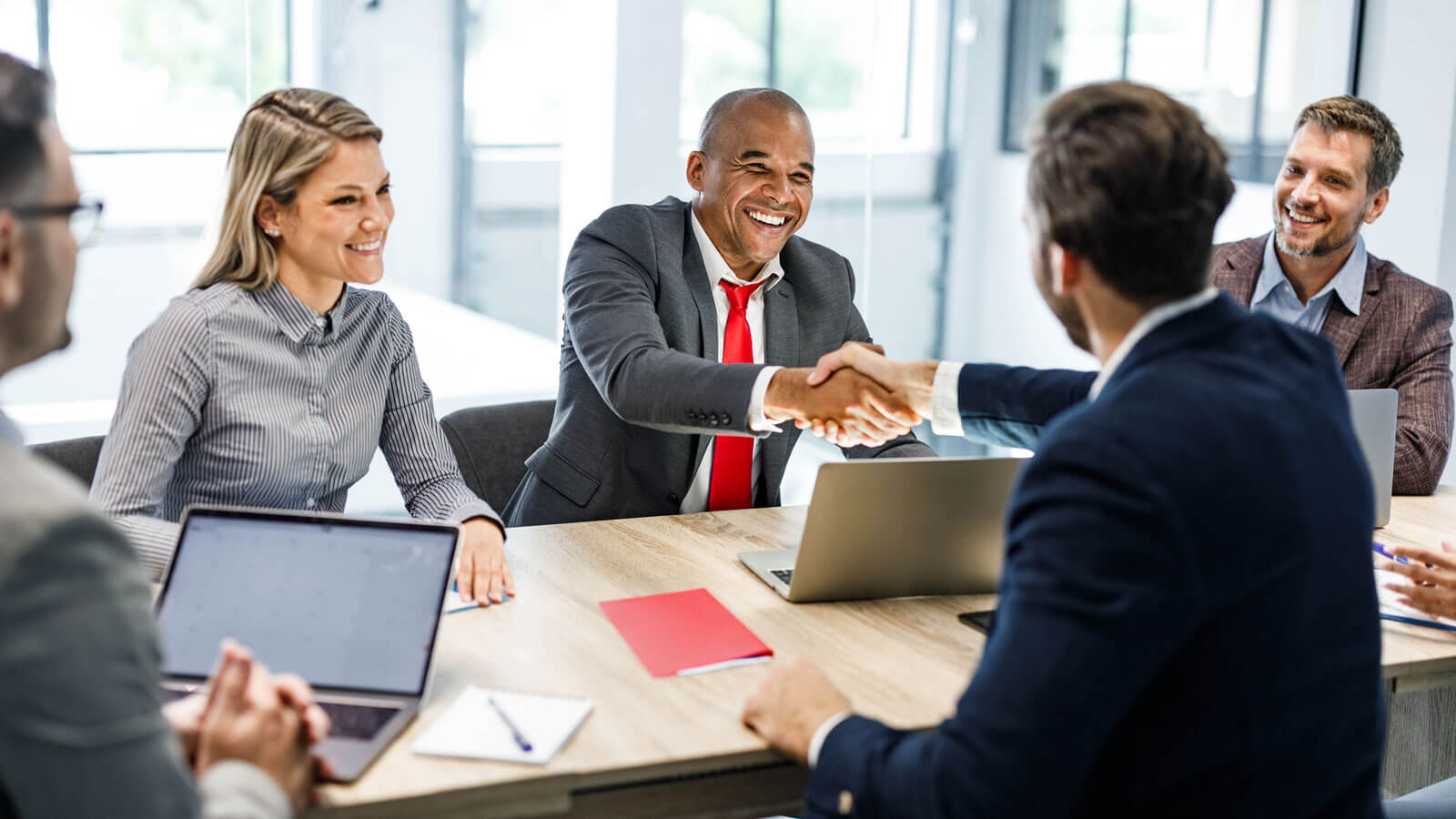 A group of four happy financial professionals sit around a conference table and shake hands with their new RIA representative after business disruption difficulties. A group of four happy financial professionals sit around a conference table and shake hands with their new RIA representative after business disruption difficulties.