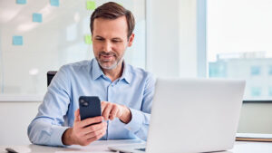 A financial professional sits at his office desk and checks social media best practices on his phone to help grow his business and engage clients.