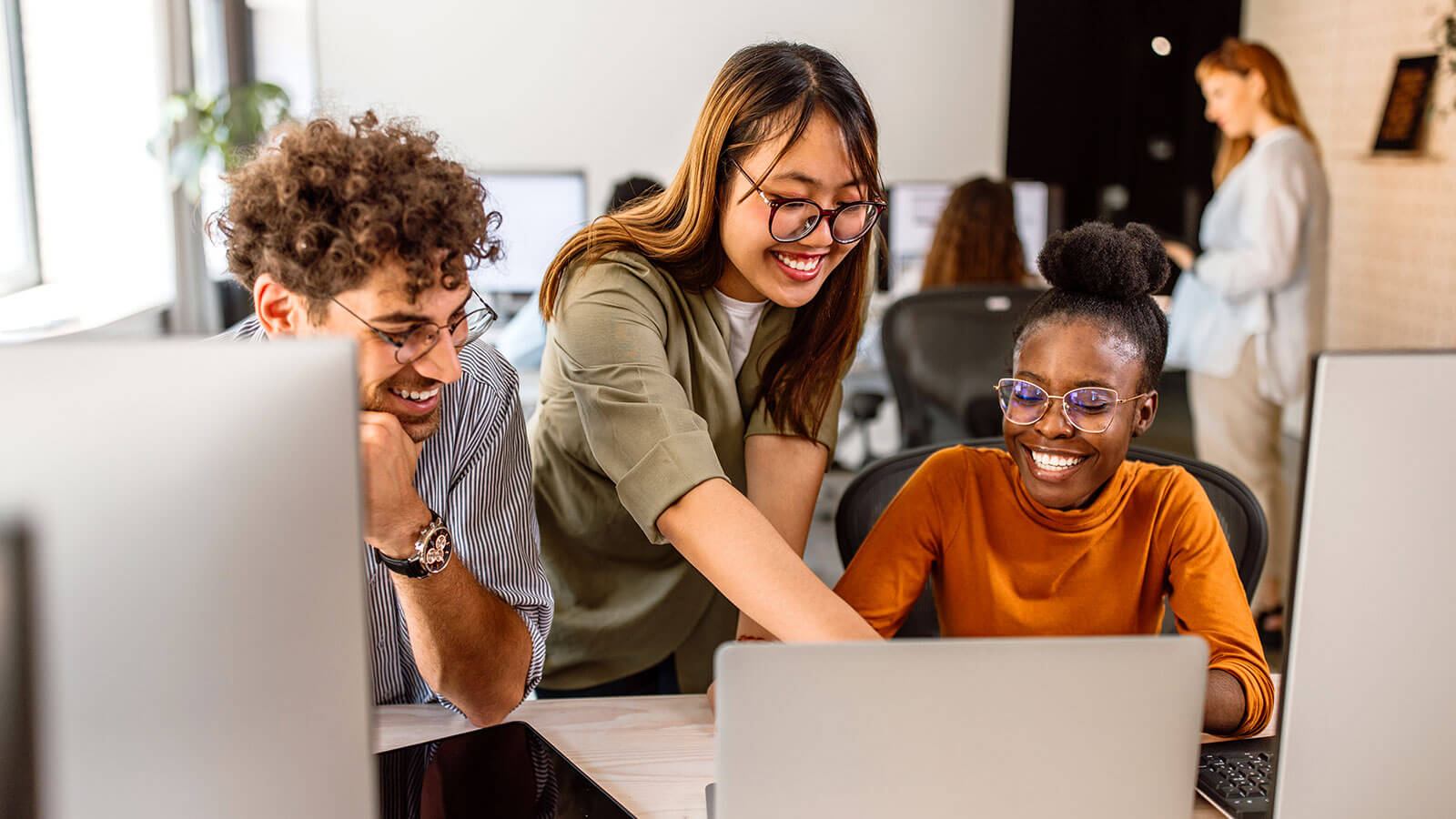 Three young professionals sit together in their workplace energetically brainstorming ideas for a project.