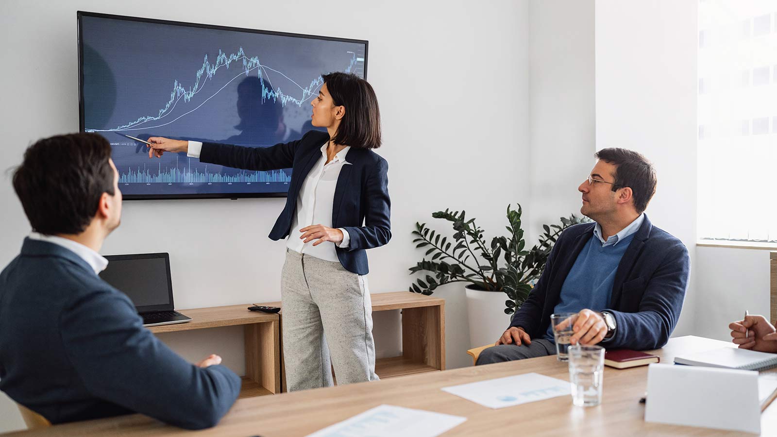 Woman pointing to screen showing graph lines.