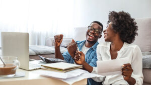 A young couple relaxes as they review their personal finances and financial tips on their laptop.