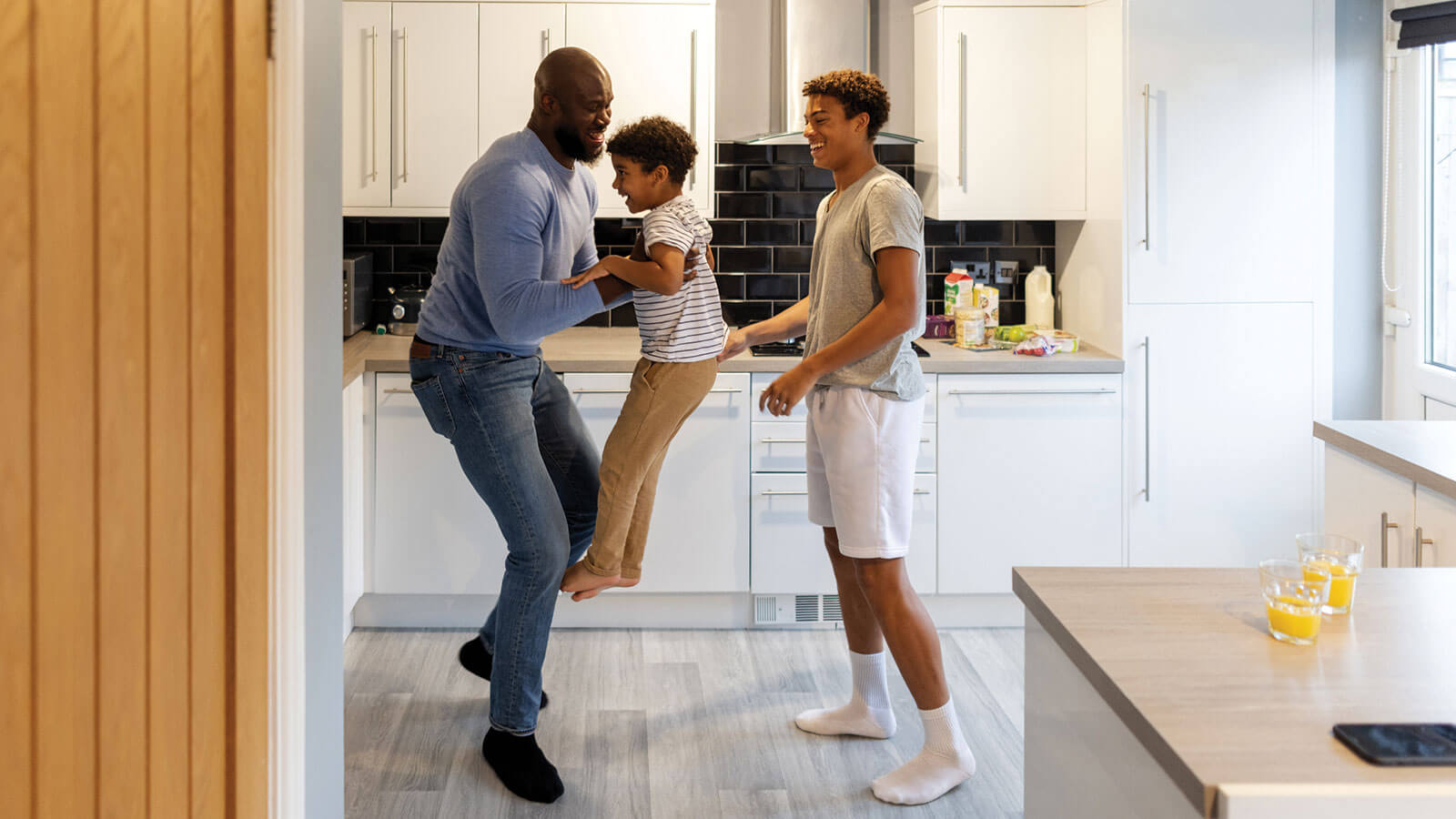 A dad plays in the kitchen with his two sons, a teenager and young boy, knowing he’s planned well with life insurance protection.