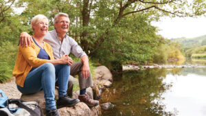 A husband and wife enjoy their retirement while hiking alongside a scenic creek view.